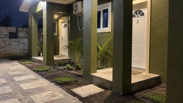 A residential building with a paved entrance, a door marked with the number 2, and a small garden area with plants.