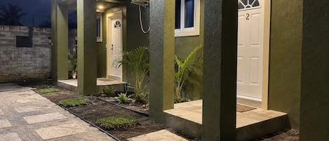 Un immeuble résidentiel avec une entrée pavée, une porte portant le numéro 2 et un petit jardin agrémenté de plantes.
