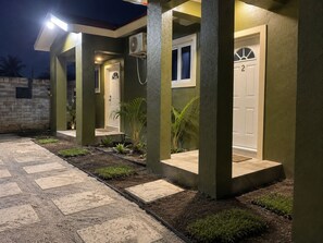 Edificio residenziale con ingresso pavimentato, una porta con il numero 2 e un piccolo giardino con piante.