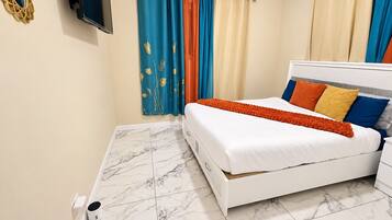 A hotel room with a white bed, a TV mounted on the wall, and a marble floor.