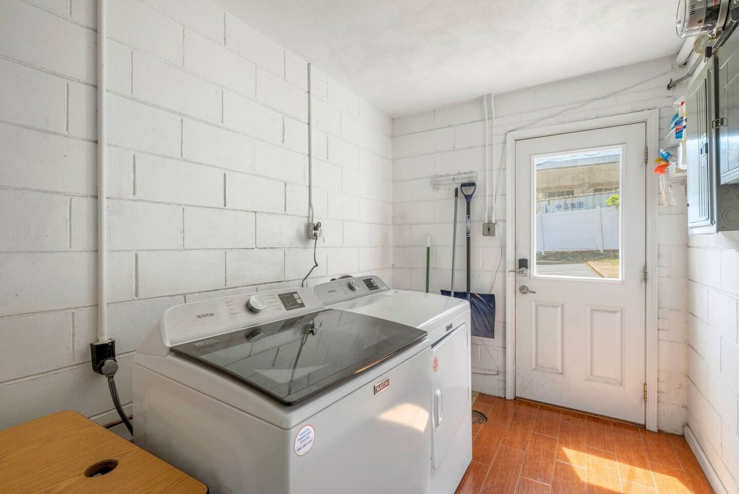 A laundry room with a front-loading washing machine, a broom, and a door leading outside.