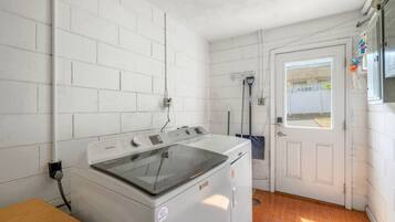 A laundry room with a front-loading washing machine, a broom, and a door leading outside.