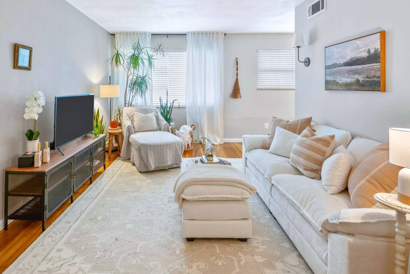 Una sala de estar con sofá, reposapiés, televisor y un ventanal con cortinas.
