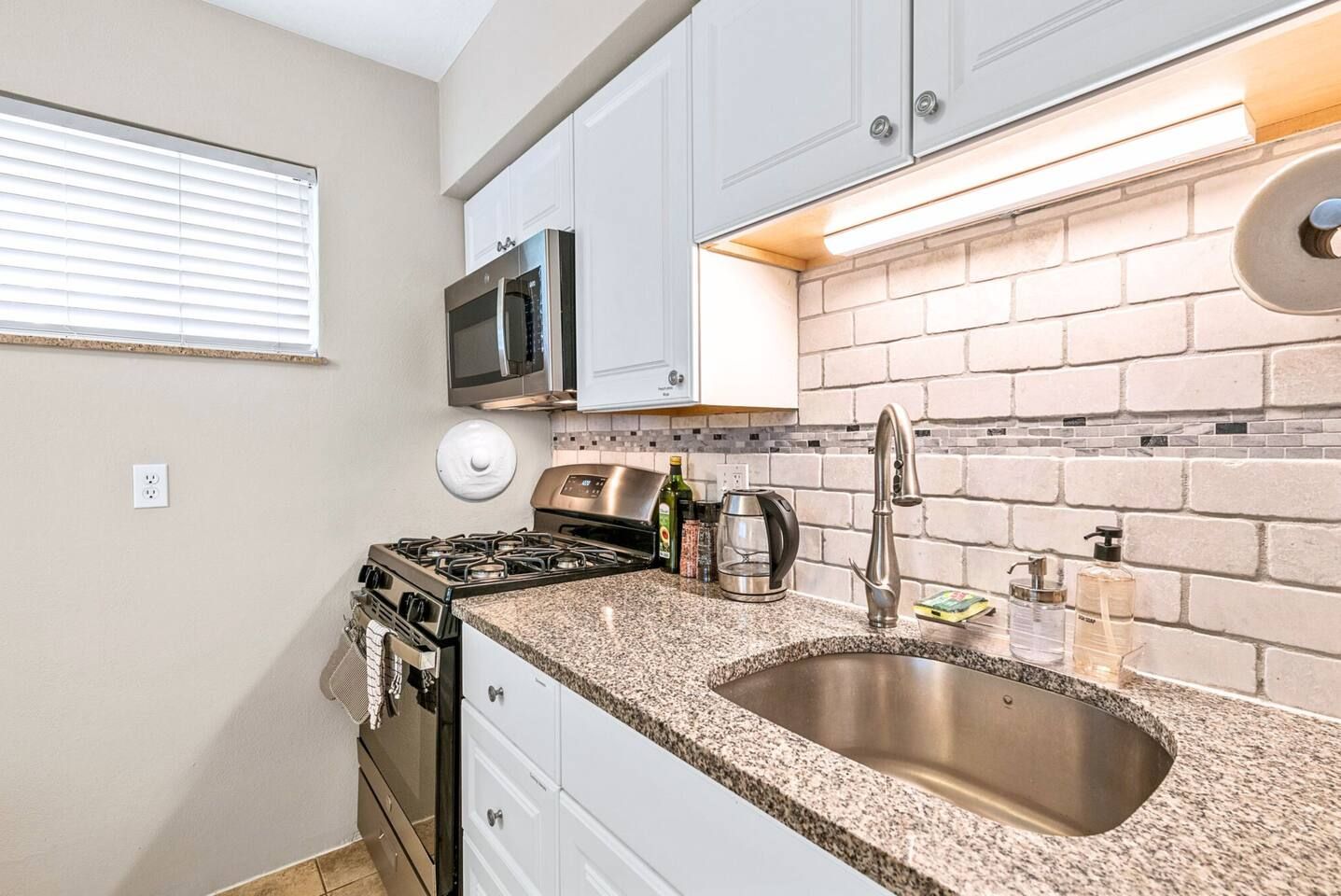 A compact kitchen with a gas stove, microwave, and a stainless steel sink.