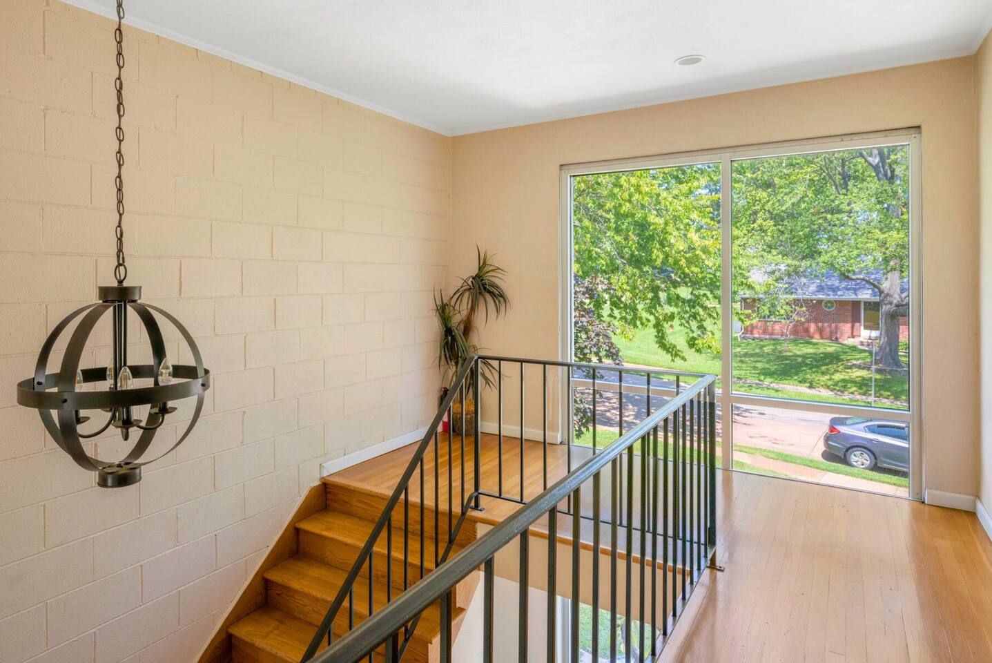 A staircase with a metal railing leading to a balcony with a large window overlooking a residential area.