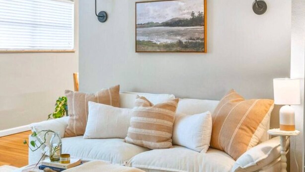 A living room with a white sofa, a painting on the wall, and a lamp on a side table. - Charming Kirkwood Two-Bedroom (St. Louis)