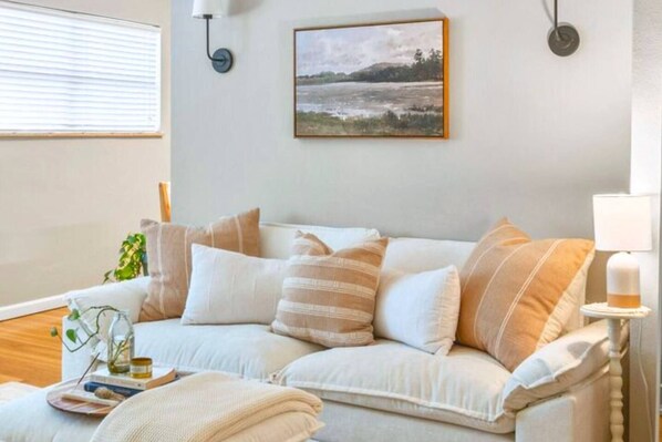Una sala de estar con un sofá blanco, un cuadro en la pared y una lámpara sobre una mesita auxiliar.