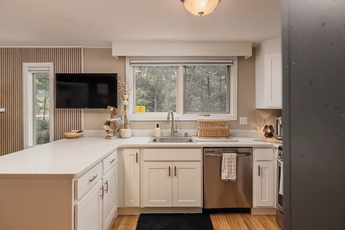 Een moderne keuken met een groot eiland, ingebouwde apparatuur en een raam met uitzicht op een bos.