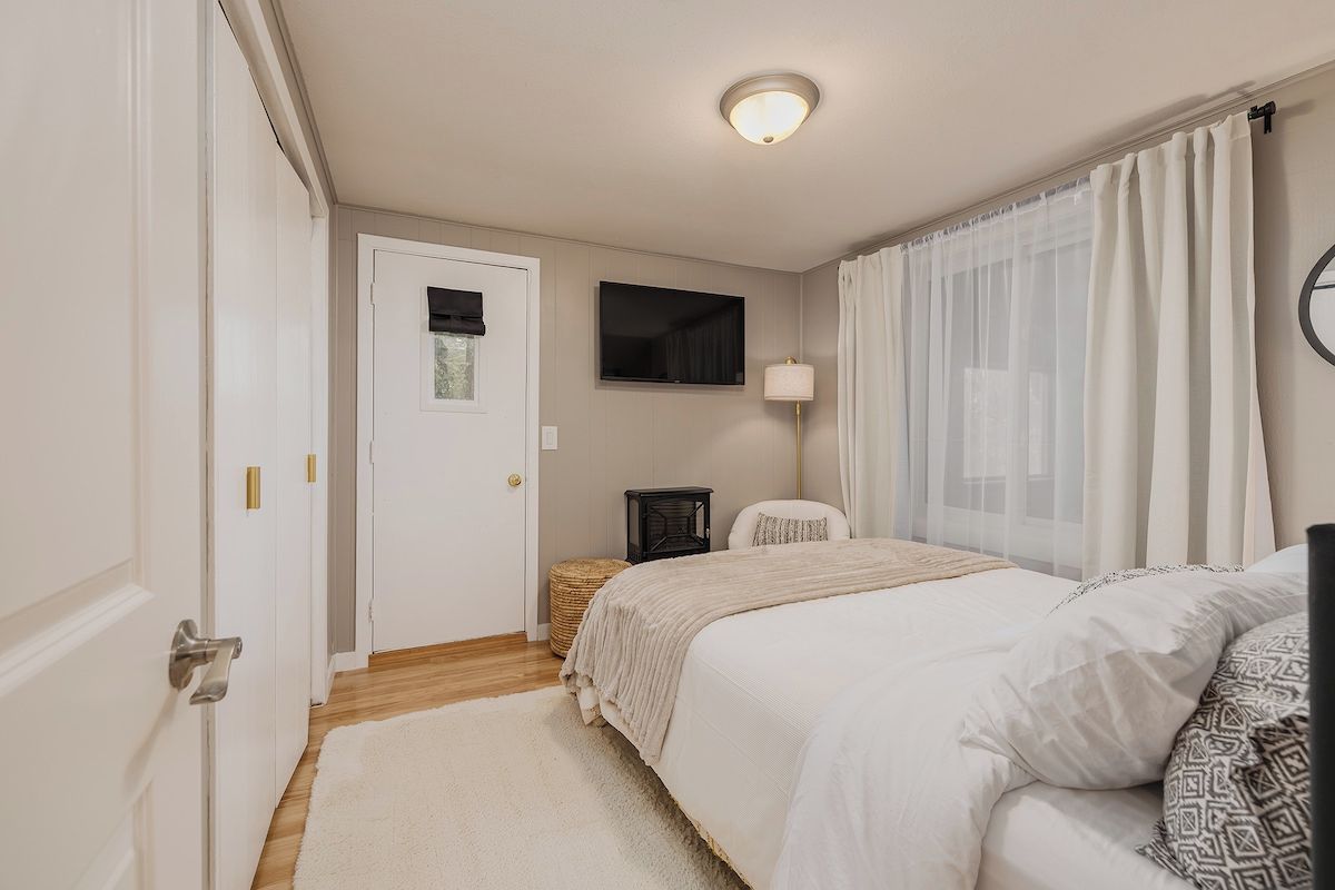 A bedroom with a bed, a bedside table, a lamp, a door, and a window with curtains.