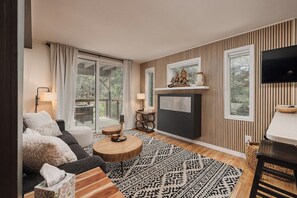 A modern living room with a sofa, coffee table, and fireplace. - Girdwood 2BR Retreat | Shared Hot Tub + Sauna (Anchorage)