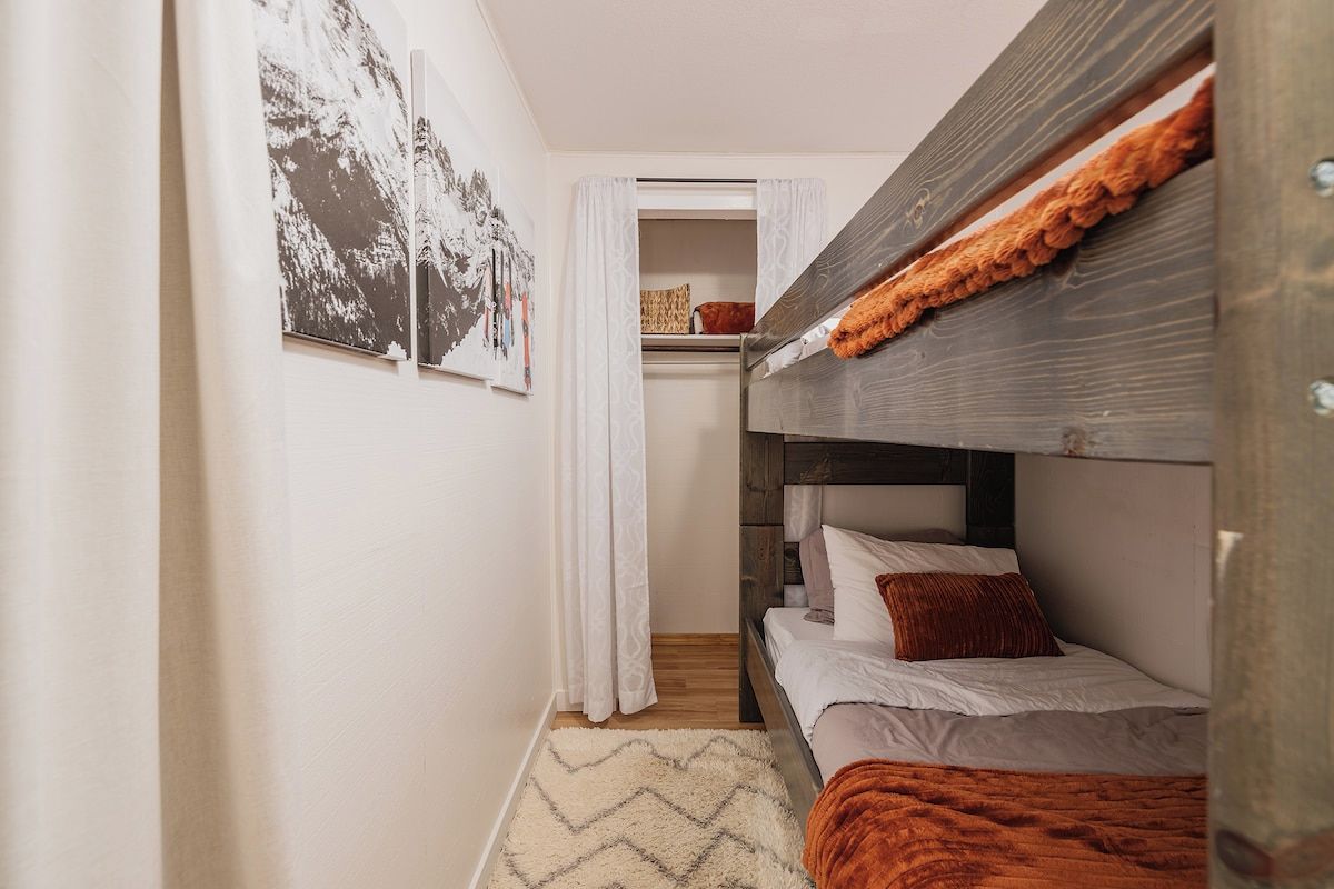 Een compacte kamer met een stapelbed, een kleine kitchenette en een deur naar een badkamer.