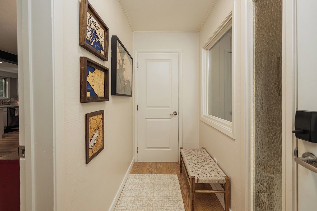 A hallway with a bench, a door, and framed artwork on the wall.