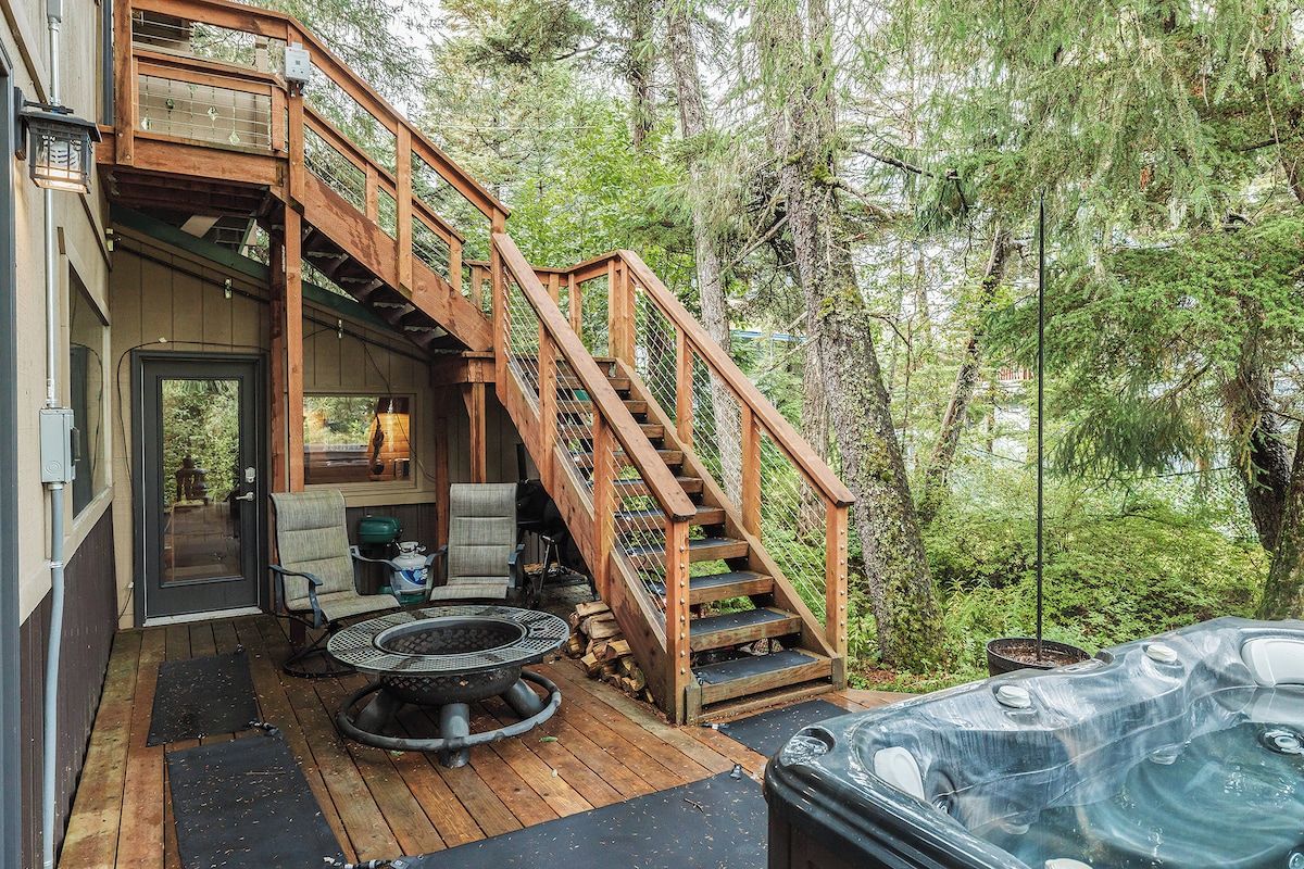 Une terrasse en bois avec un jacuzzi, des sièges d’extérieur et un escalier menant à une zone abritée.