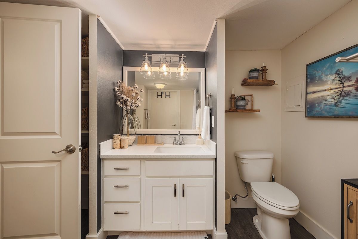 A bathroom with a white vanity, a mirror, a toilet, and a painting on the wall.