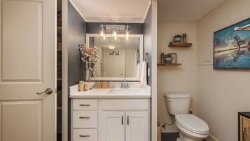 A bathroom with a white vanity, a mirror, a toilet, and a painting on the wall.
