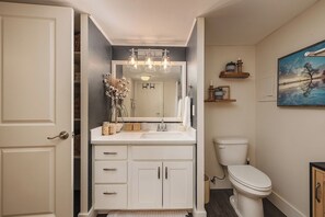 A bathroom with a white vanity, a mirror, a toilet, and a painting on the wall. - Girdwood 2BR Retreat | Shared Hot Tub + Sauna (Anchorage)