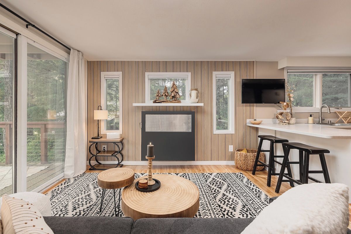 A modern living room with a fireplace, a television, and a kitchen area with stools.