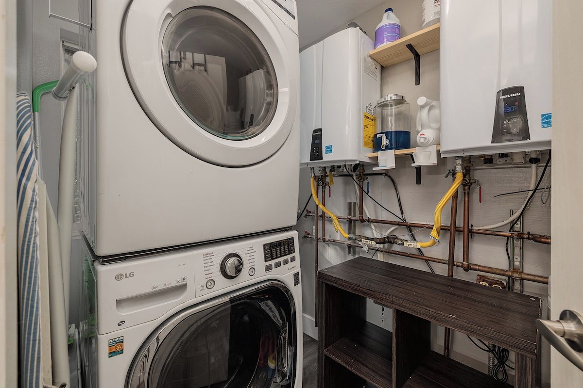 A laundry area with stacked washing machines, a water heater, and various plumbing pipes.
