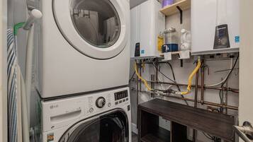 A laundry area with stacked washing machines, a water heater, and various plumbing pipes.