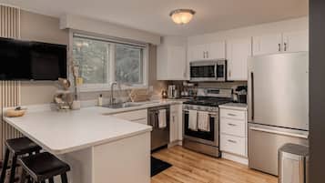 A modern kitchen with white cabinetry, stainless steel appliances, a large window, and a flat-screen TV mounted above the counter.
