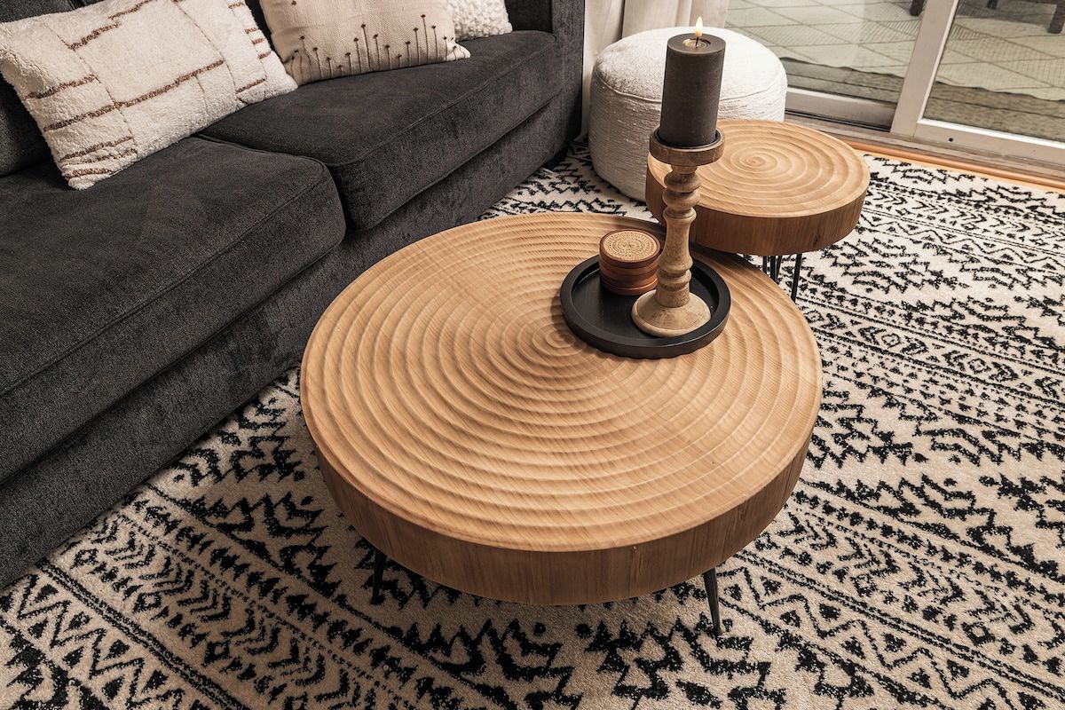 Een ronde houten salontafel met kandelaar, een kamerbreed tapijt en een donkere bank in een woonkamer.