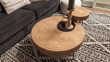 Een ronde houten salontafel met kandelaar, een kamerbreed tapijt en een donkere bank in een woonkamer.