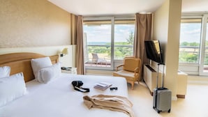 A hotel room with a bed, a TV, a chair, a suitcase, and a view of the outdoors. - Hotel Les Dryades Golf & Spa (Pouligny-Notre-Dame)