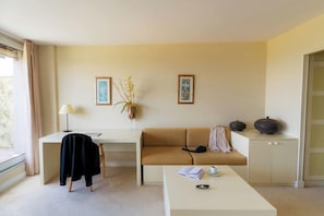 A modern living room with a sofa, a coffee table, a desk, and a lamp. There are two framed pictures on the wall. - Hotel Les Dryades Golf & Spa (Pouligny-Notre-Dame)