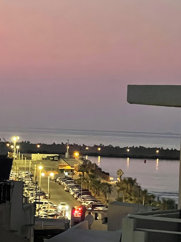 A parking lot with cars and a view of the sea at dusk.