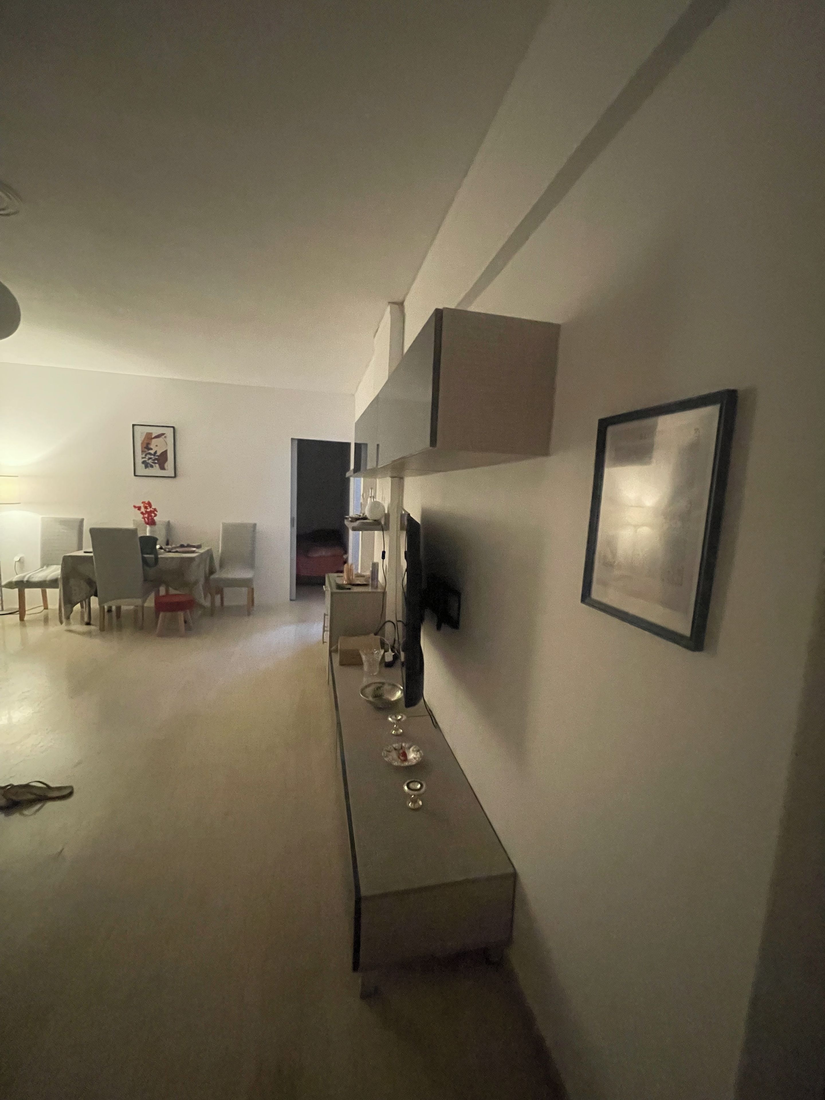 A modern living room with a dining area, a sofa, a coffee table, and a TV mounted on the wall.