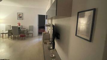 A modern living room with a dining area, a sofa, a coffee table, and a TV mounted on the wall.