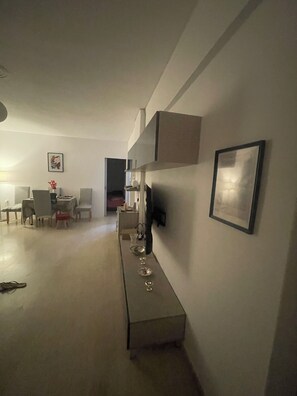 A modern living room with a dining area, a sofa, a coffee table, and a TV mounted on the wall.