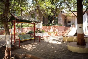 Un patio exterior con un columpio, un espacio de descanso cubierto y una escalera que lleva a un nivel superior.
