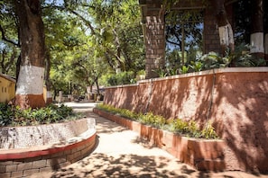 A pathway flanked by a brick wall and trees, leading to a building with a brick facade. - Adamo Village (Karjat)