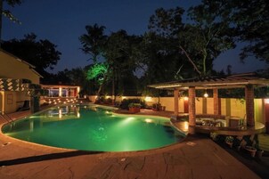 Una piscina con un área de estar hundida, rodeada por un patio con plantas en macetas y un pérgola con luces.
