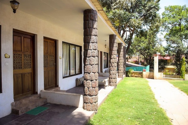 A building with stone pillars, wooden doors, and a green mat at the entrance. - Adamo Village (Karjat)