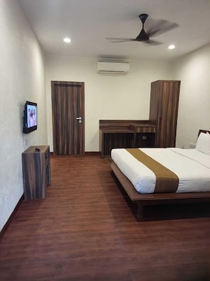 A hotel room with a bed, a desk, a television, and a wardrobe. - Adamo Village (Karjat)