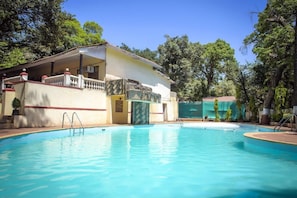 A swimming pool with a covered area, surrounded by trees. - Adamo Village (Karjat)