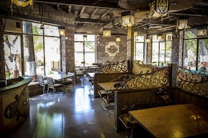 An interior with a mix of rustic and modern design, featuring a central seating area with ornate metal railings, tables, and chairs arranged around it. - Adamo Village (Karjat)
