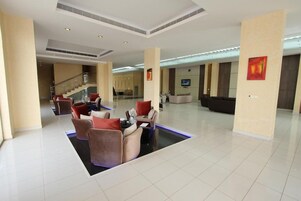 Un vestíbulo amplio con una zona de estar central, una escalera y una recepción.