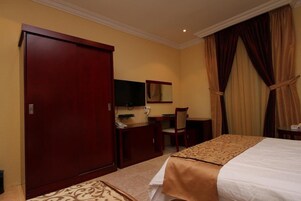 Una habitación de hotel con cama, escritorio, silla, armario y televisor.