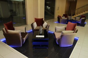 A lobby area with a central seating arrangement, a staircase, and a glass wall.