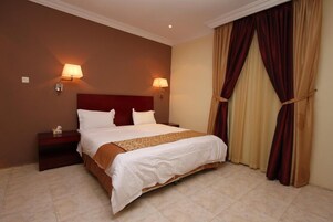 Habitación de hotel con una cama individual, dos lámparas de noche, una mesita de noche y un ventanal con cortinas.