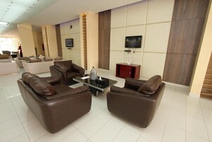 A modern living room with leather sofas, a glass coffee table, and a flat-screen TV mounted on the wall.