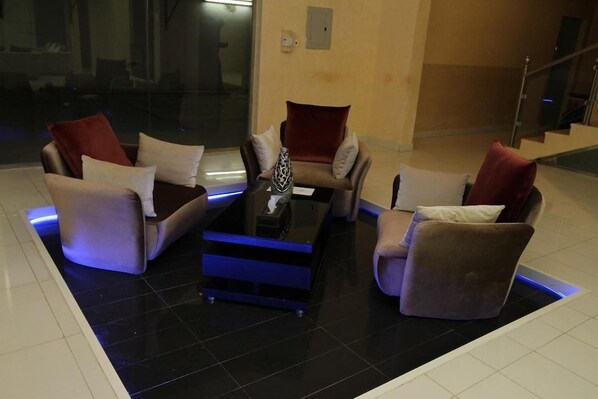 A modern lounge area with a black coffee table, two sofas with red and white cushions, and a glass partition.