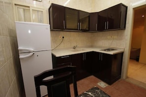 Uma cozinha compacta com armários escuros, uma geladeira branca e uma pia.