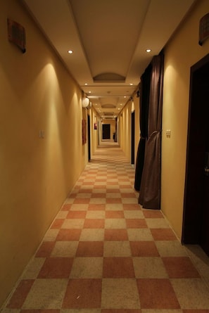 A hotel corridor with checkered flooring, doors on both sides, and recessed lighting.
