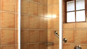 Box doccia con porta in vetro, toilette e finestra sopra la doccia.