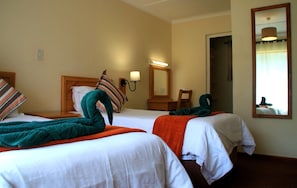 A hotel room with two beds, a nightstand, a mirror, and a lamp.