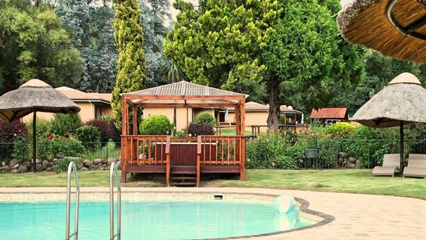 Una piscina con un pontile in legno e un gazebo, immersa nel verde e ombreggiata da parasoli di paglia.